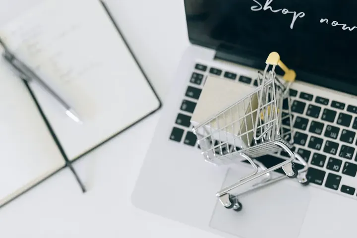 Carrinho de compras em miniatura sobre um notebook com a mensagem Shop now